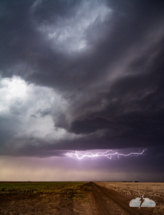 The tiny wall cloud sculpted by the downdraft, with lightning.