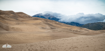 A panorama of the dunes and the cloud-capped mountains beyond.