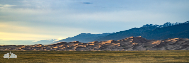 A panoramic crop brings out the detail of the dreamy dunes at sunset. Wind blows sand off the crests.