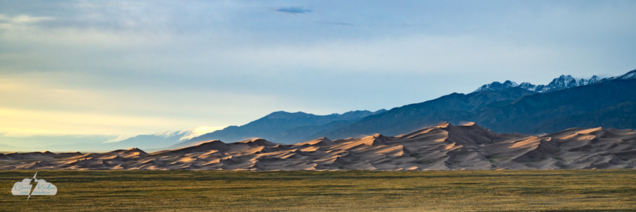 A panoramic crop brings out the detail of the dreamy dunes at sunset. Wind blows sand off the crests.