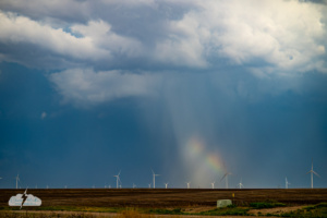 A brief hailbow flashes with color under a storm.