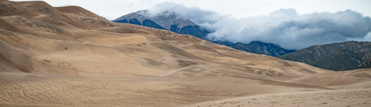 A panorama of the dunes and the cloud-capped mountains beyond.