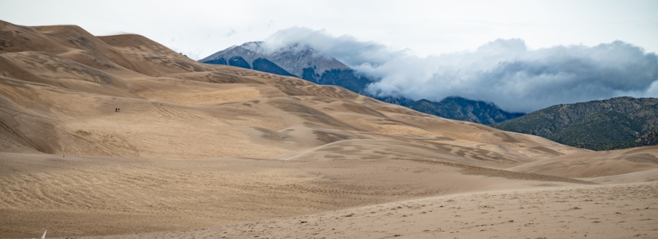 A panorama of the dunes and the cloud-capped mountains beyond.